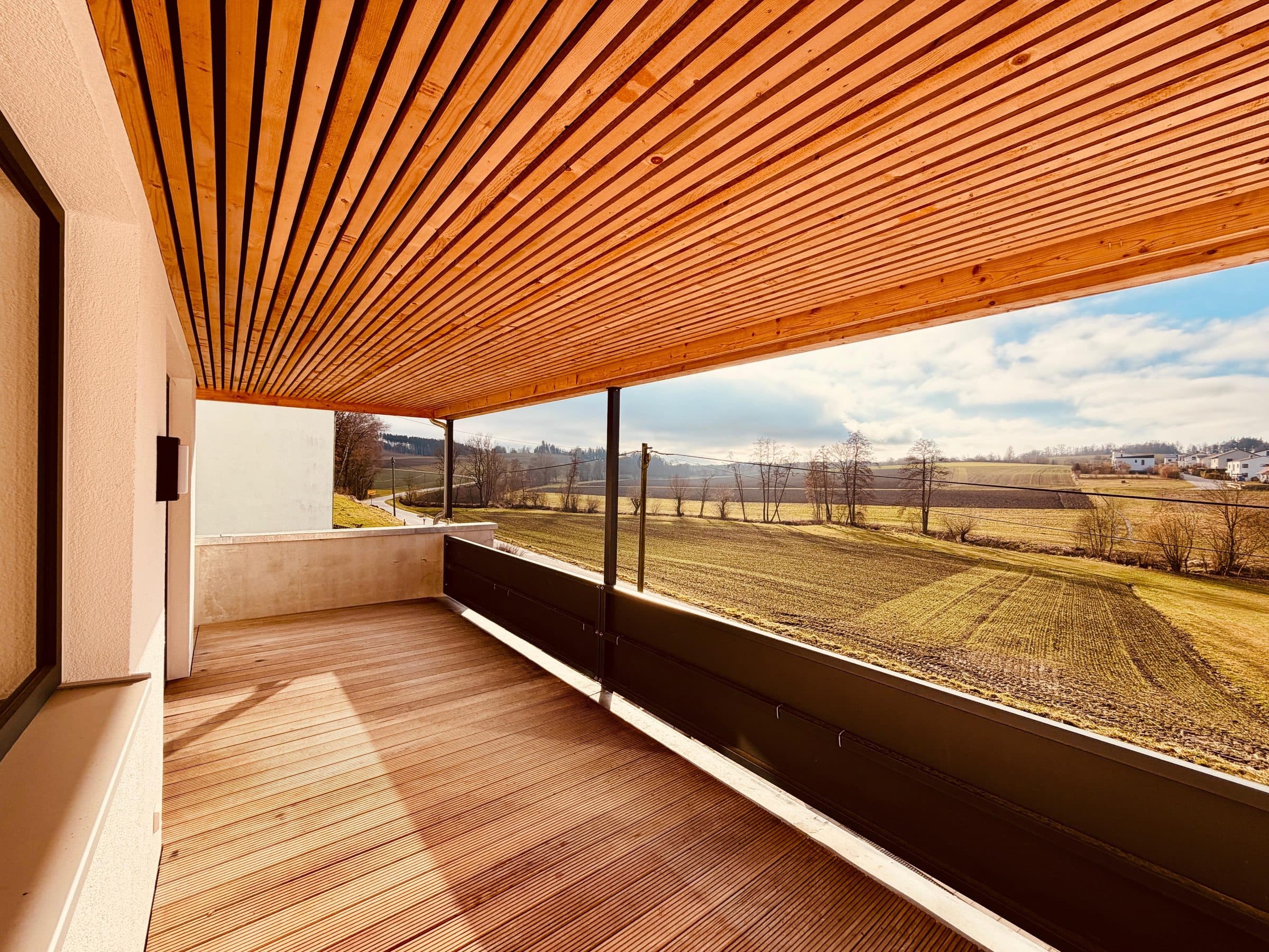 Überdachte Holzterrasse einer ROOM4U-Unterkunft mit weitem Blick über Felder und Hügel