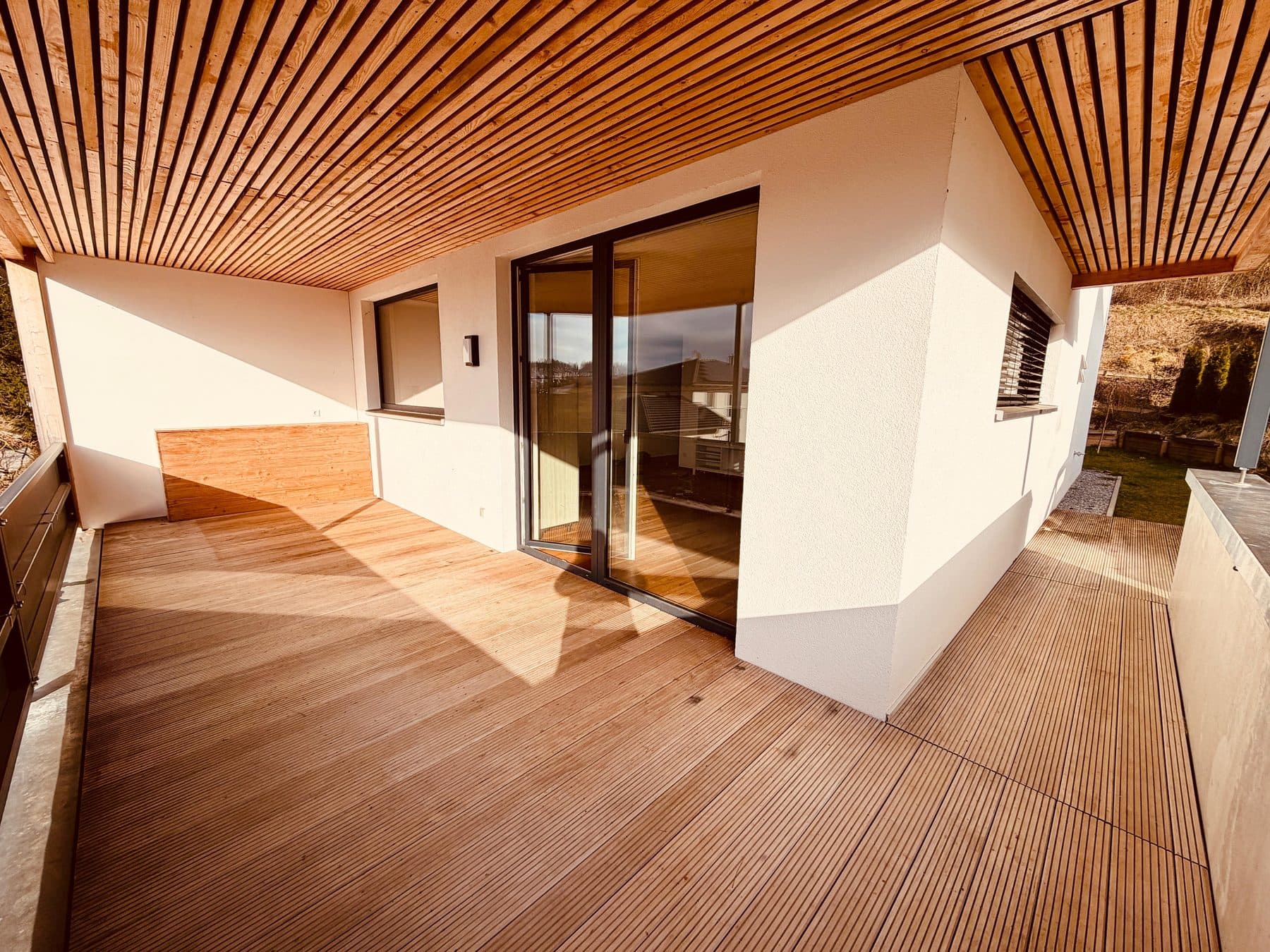Außenansicht einer ROOM4U-Unterkunft mit überdachter Holzterrasse und Zugang zur Wohnung